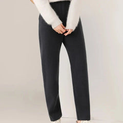 Person wearing a white fuzzy sweater and black straight-leg pants with a slim tailored leg, standing against a plain light-colored background. Their hands are clasped in front, and only the lower half of their body is visible.