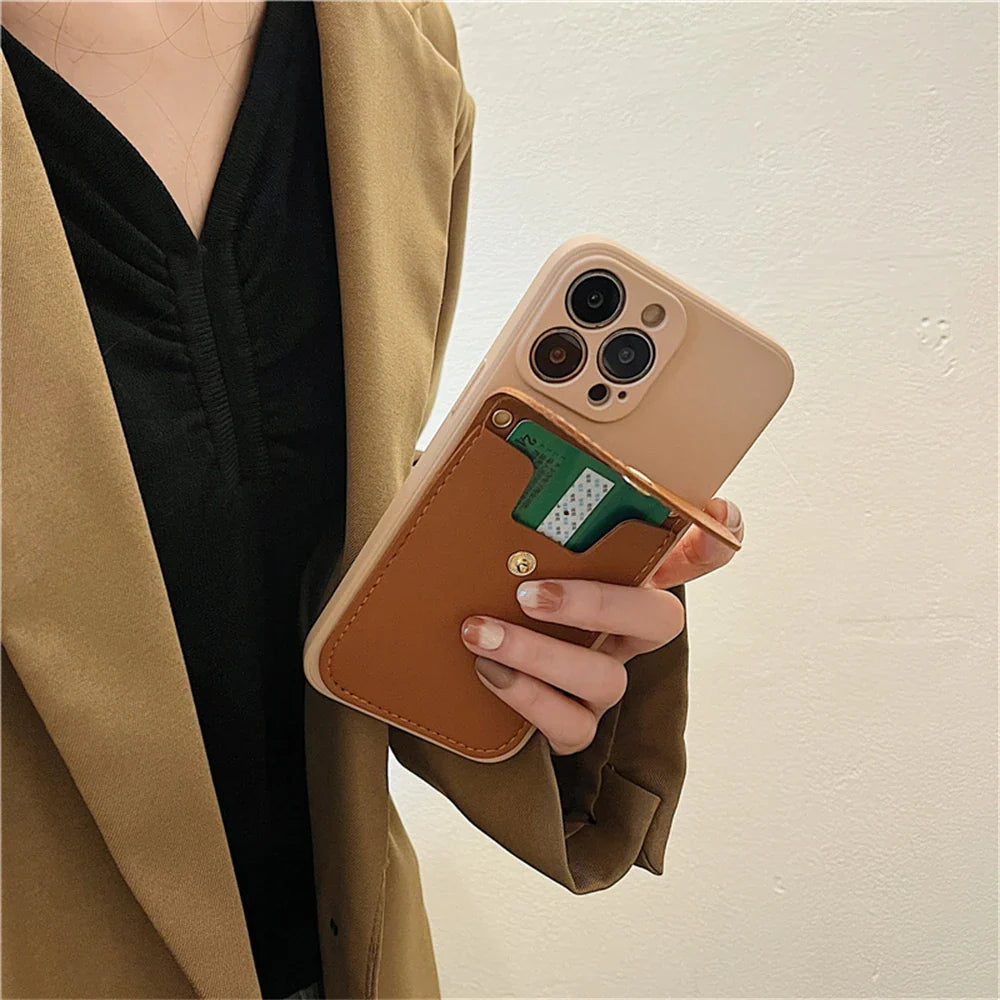 A person wearing a brown blazer and black top holds a beige smartphone with a phone case wallet featuring a secure cardholder and brown wallet case, against a plain light-colored wall.
