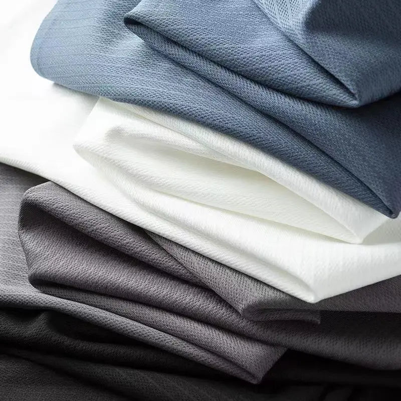 A close-up of stacked fabric in shades of gray, white, and blue, showing their smooth, slightly textured surfaces and soft folds—ideal for crafting a men's slim shirt or business casual shirt.