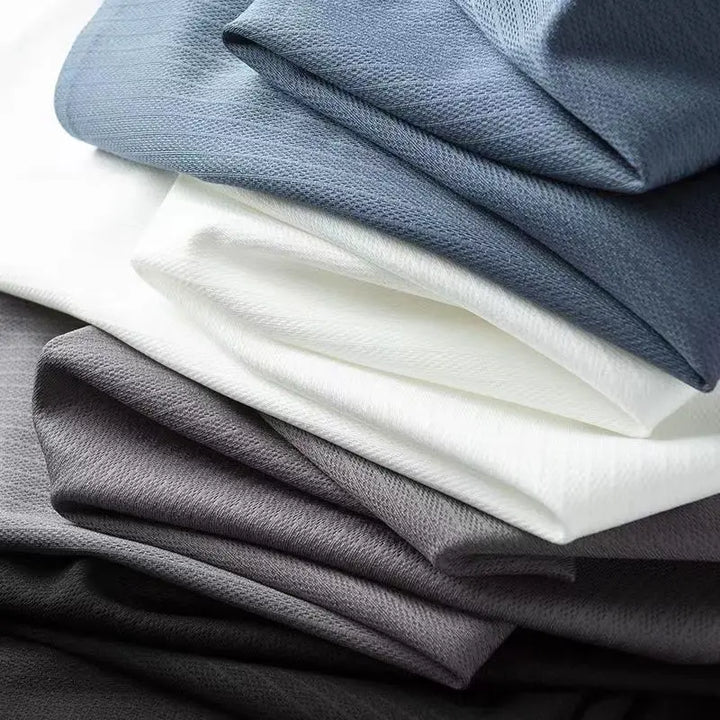 A close-up of stacked fabric in shades of gray, white, and blue, showing their smooth, slightly textured surfaces and soft folds—ideal for crafting a men's slim shirt or business casual shirt.
