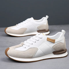 A pair of white and beige sneakers with brown accents and white laces, crafted from top-grain leather, displayed on a gray surface with a plain gray background.