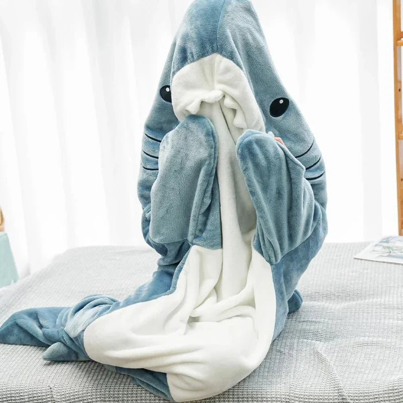 A plush blanket shaped like a blue and white shark is draped upright on a chair, with the sharks adorable face and fins visible, resembling cozy pajamas with its soft fabric and invitingly warm appearance.