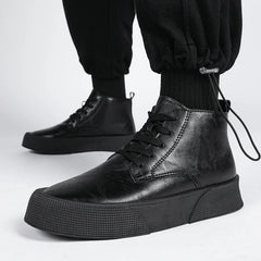 A person wears black vintage-inspired high-tops with thick soles and black laces, paired with black jogger pants. The photo focuses on the shoes cushioned footbed against a plain white background.