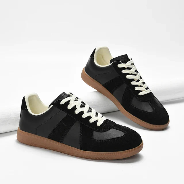 A pair of black sneakers with white laces, premium cow suede accents, white inner lining, and brown rubber soles, displayed on a white background.