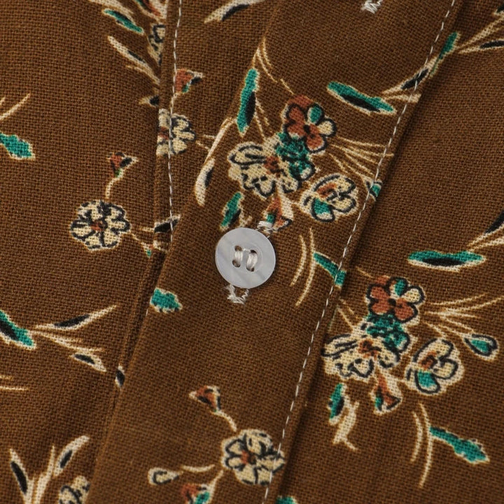 Close-up of a classic design cotton shirt in brown fabric with a floral pattern in cream, green, and maroon, featuring a white button and visible stitching along the seam.