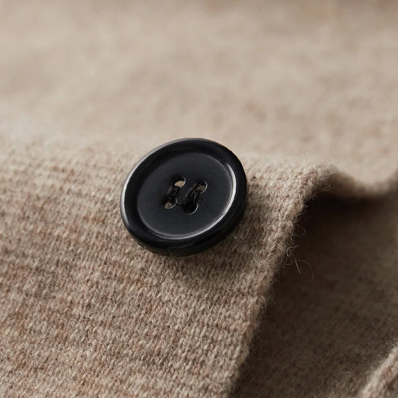 A close-up of a black, four-hole button sewn onto a textured, light brown fabric, likely part of a tailored cardigan. The button sits near the edge of the soft, slightly woolly material.