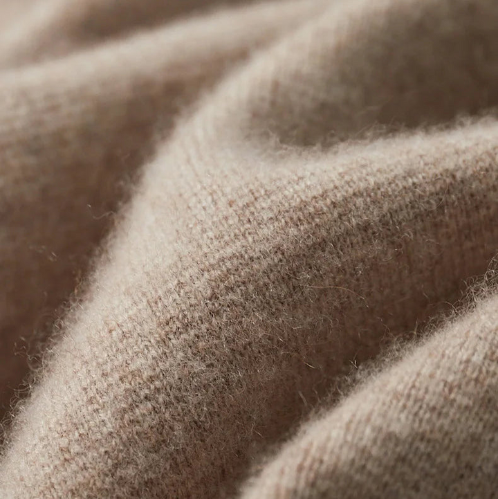 Close-up of soft, beige wool or premium cashmere cardigan fabric, showing its fuzzy texture and gentle folds.