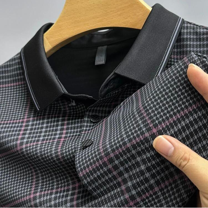 A hand holds a black and white checkered long-sleeve shirt with a black collar on a wooden hanger. The breathable shirt features a subtle pink plaid pattern, buttoned front, and is perfect for temperature-regulating comfort.