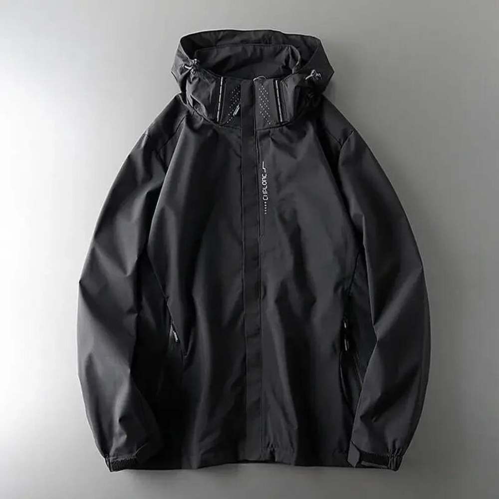 A black windproof jacket with a zipper and high collar is laid flat on a neutral gray surface. The material appears to be waterproof or water-resistant with subtle stitching details.