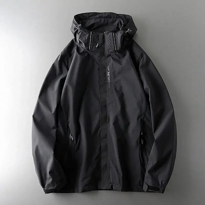 A black windproof jacket with a zipper and high collar is laid flat on a neutral gray surface. The material appears to be waterproof or water-resistant with subtle stitching details.