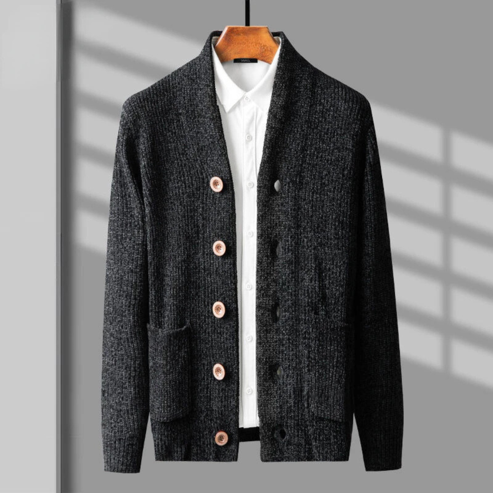 A dark gray knit cardigan in a button up style with light brown buttons is layered over a white collared shirt. Both are hanging on a wooden hanger against a gray background with diagonal shadow lines.