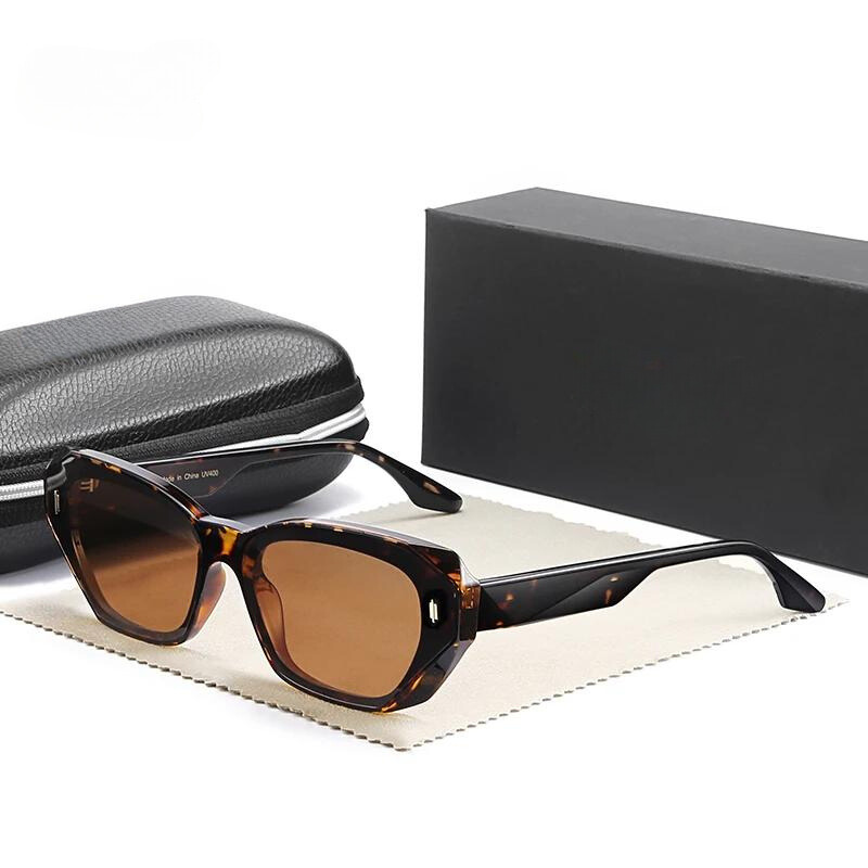 Tortoiseshell Cat Eye Sunglasses with brown lenses are displayed on a beige cloth, next to a black zippered case and a black rectangular box.