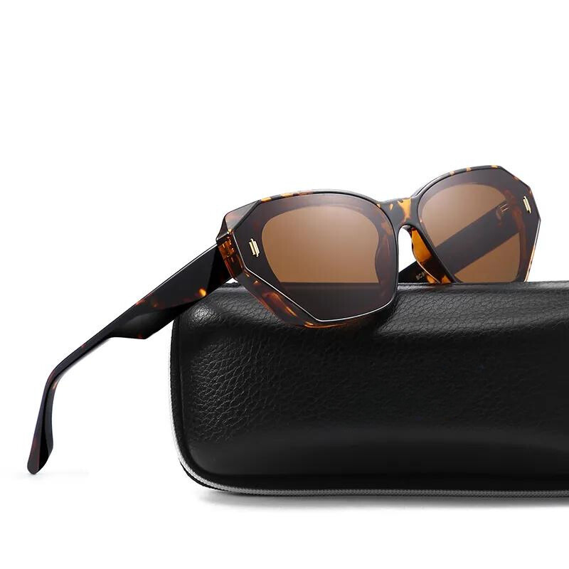 A pair of brown, geometric-shaped tortoiseshell cat eye sunglasses with brown lenses is resting on top of a black leather sunglasses case.