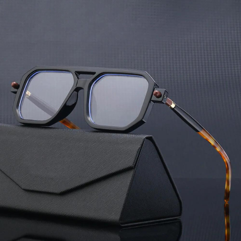 A pair of luxury eyewear with a geometric, oversized black silhouette and tortoiseshell arms rests on a black textured case against a dark, patterned background.