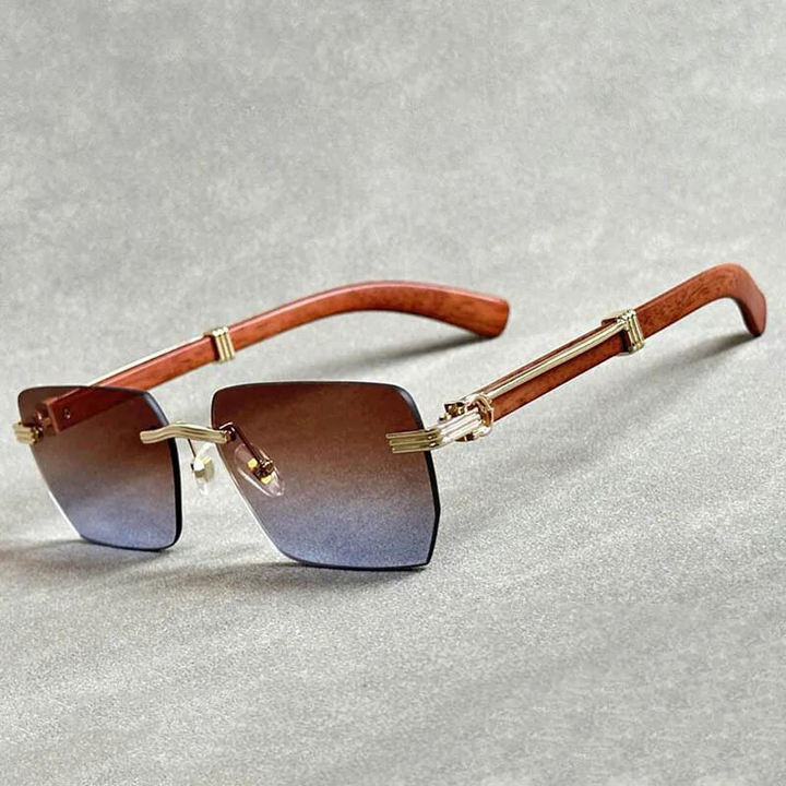 A pair of rimless sunglasses with gradient lenses, gold metal accents, and wooden temples, displayed on a light gray surface.