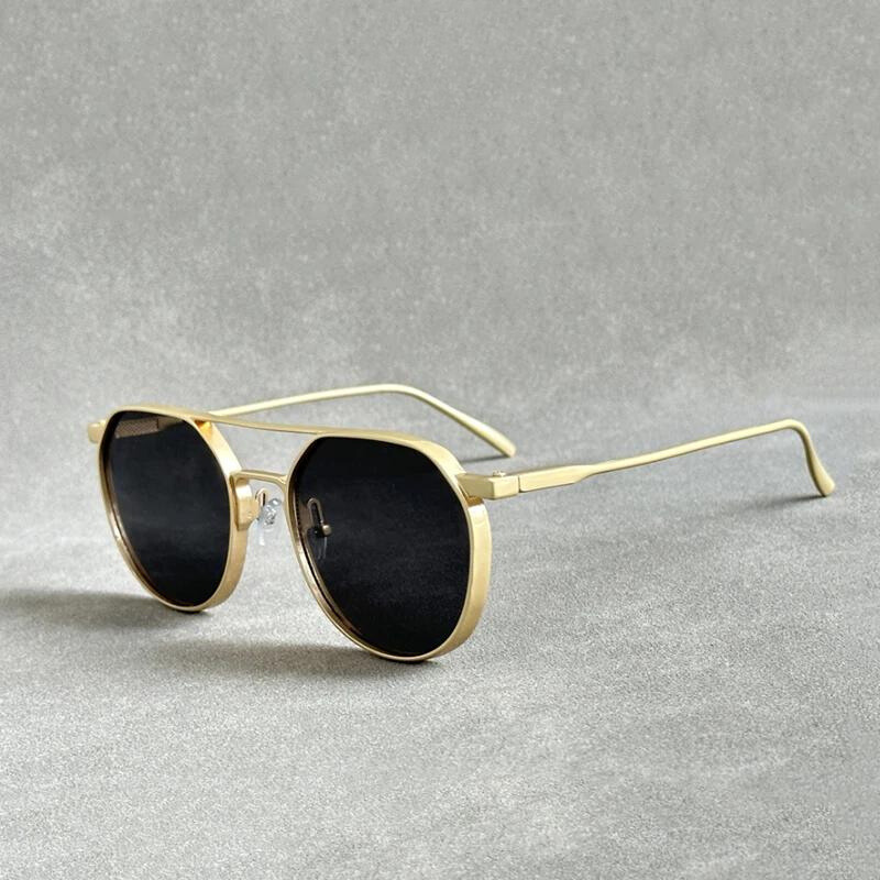 A pair of gold-framed sunglasses with black lenses, crafted from lightweight alloy and offering UV400 protection, is displayed on a light gray textured surface, with one temple arm resting flat and the other slightly raised.