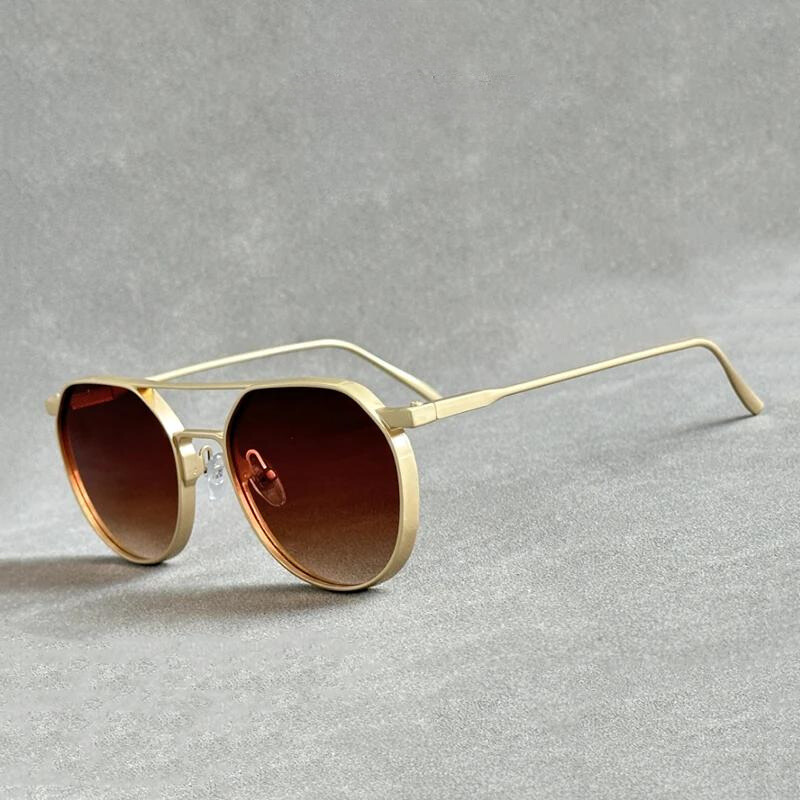 Gold-framed aviator sunglasses with brown gradient lenses placed on a textured gray surface. Crafted from lightweight alloy, these sunglasses feature thin, slightly curved arms and offer UV400 protection for stylish, reliable wear.