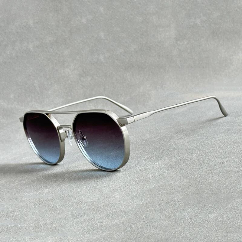 A pair of silver-framed aviator sunglasses crafted from lightweight alloy with dark gradient lenses and UV400 protection, resting on a gray textured surface.