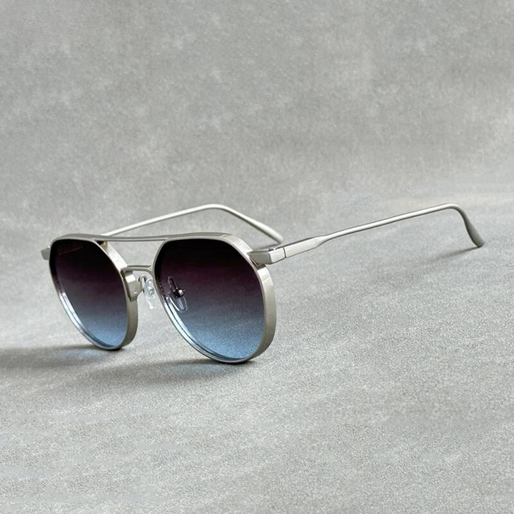 A pair of silver-framed aviator sunglasses crafted from lightweight alloy with dark gradient lenses and UV400 protection, resting on a gray textured surface.