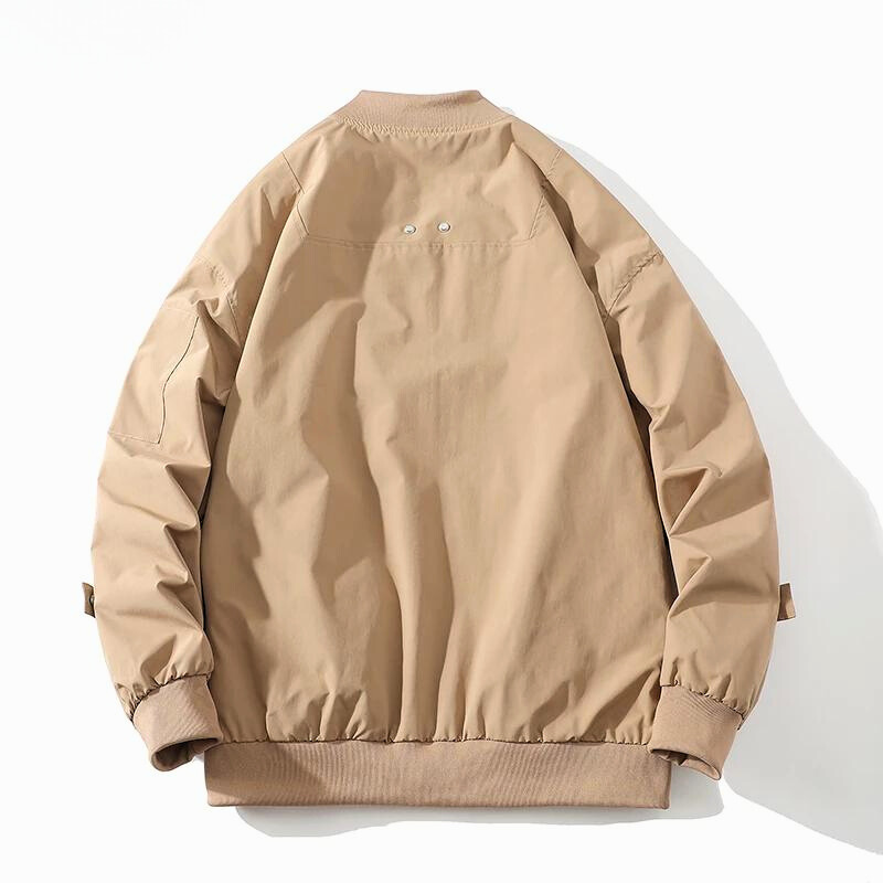 A light brown bomber jacket with a classic design is laid flat, back facing up, showing ribbed cuffs and hem, small eyelets near the shoulders, a ribbed collar, and adjustable straps on the sleeves.