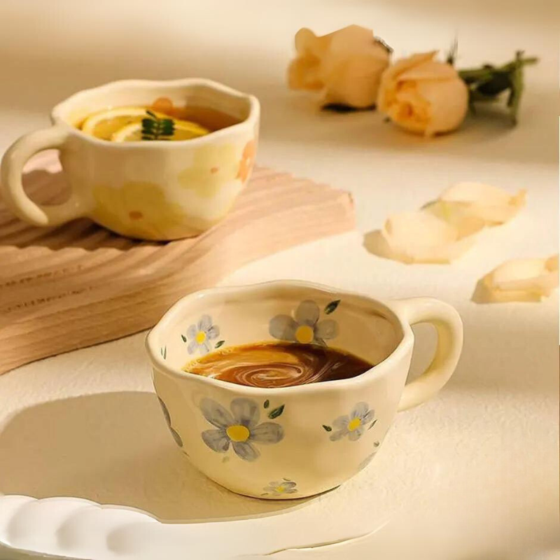 Two vintage teacups with painted flower designs sit on a light surface. One holds coffee, the other a drink with lemon slices. Pale peach roses and petals in the background add to the soft, warm atmosphere.