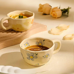 Two vintage teacups with painted flower designs sit on a light surface. One holds coffee, the other a drink with lemon slices. Pale peach roses and petals in the background add to the soft, warm atmosphere.