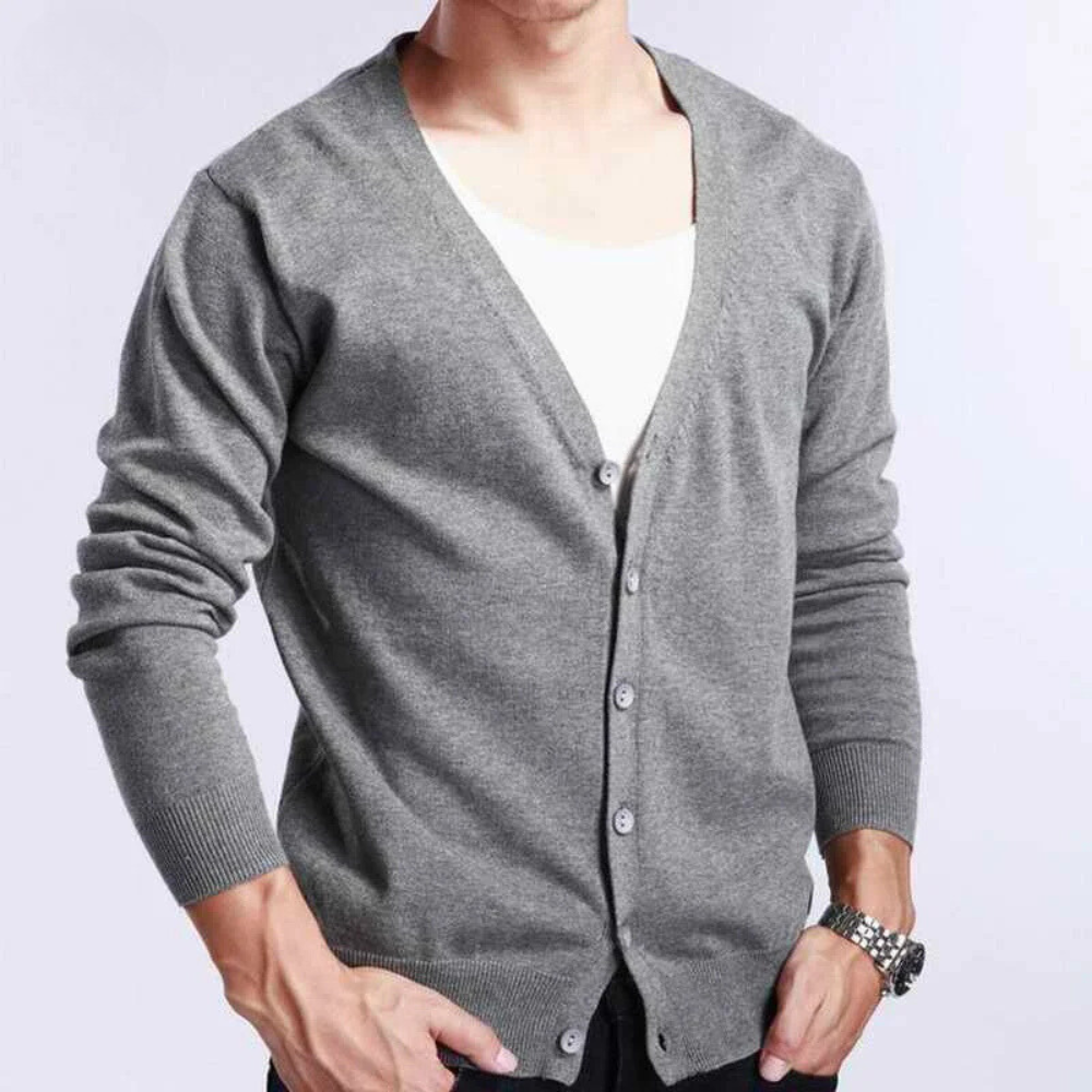 A person wearing a light gray, V-neckline button-up cardigan in a relaxed fit over a white shirt, with sleeves pushed up slightly, stands against a plain light background. Only the torso and arms are visible.