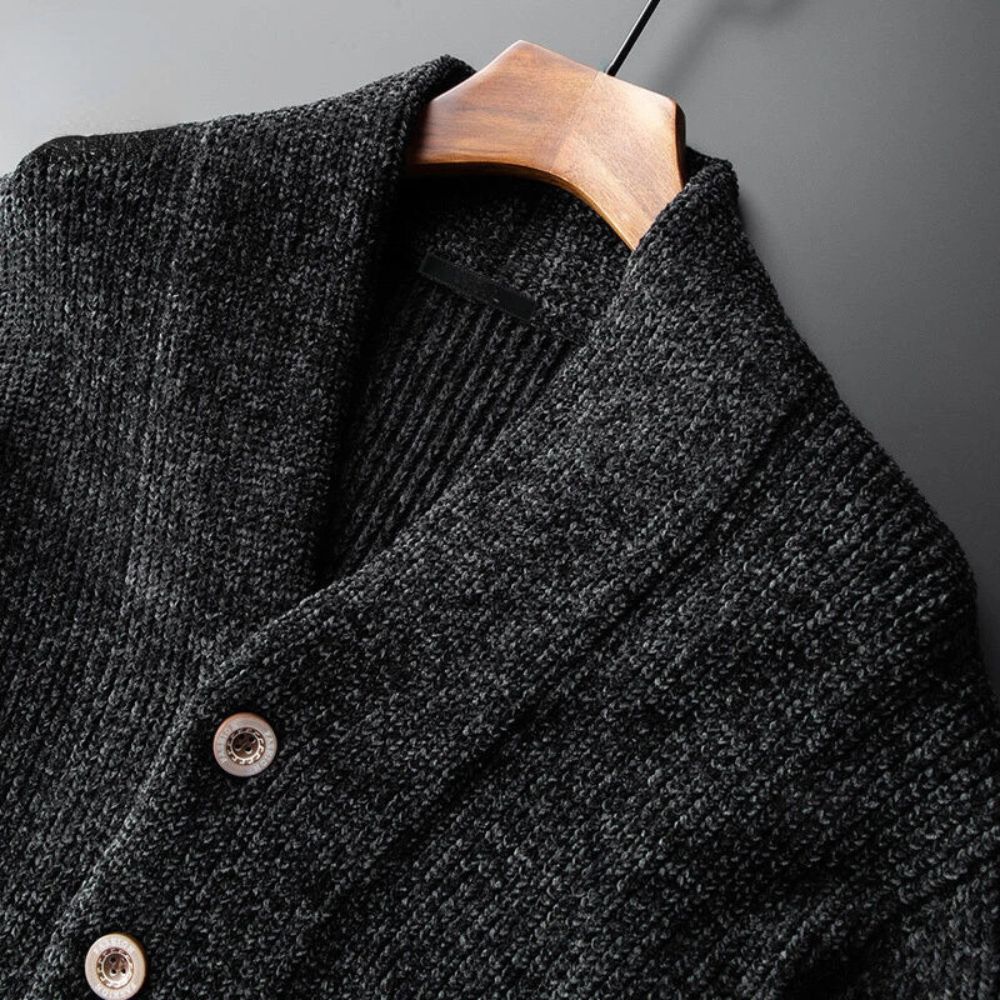 Close-up of a textured dark gray cashmere wool blend knit cardigan with a shawl collar, two visible buttons, and displayed on a wooden hanger against a dark background—perfect for layering in button up style.