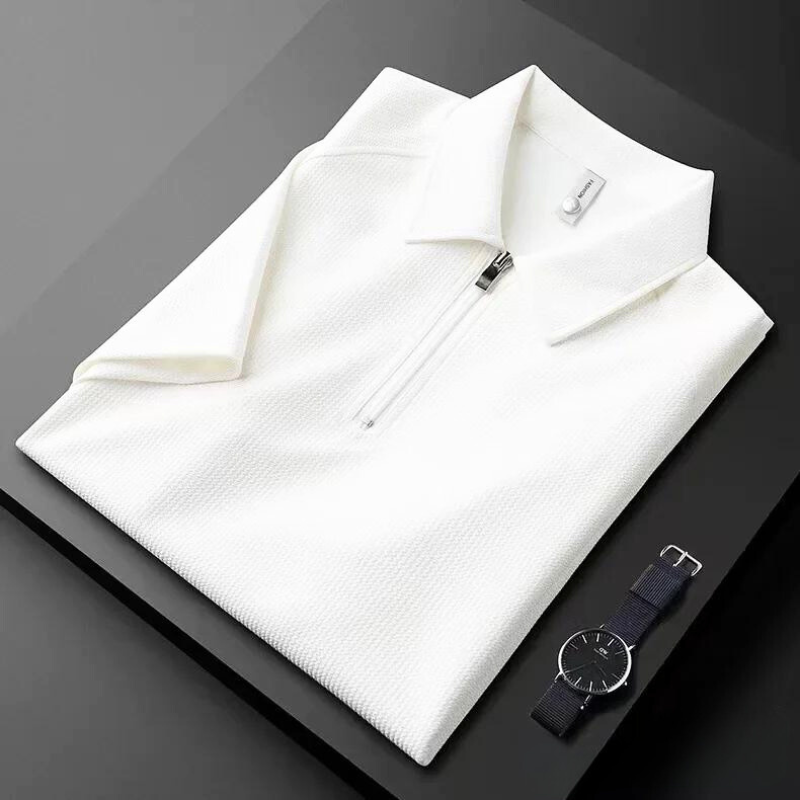 A neatly folded white mens silk polo shirt with a front zipper is placed on a black surface next to a minimalist black wristwatch with a black strap.