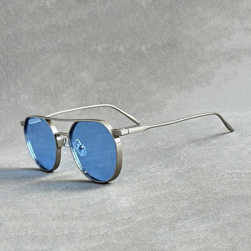 A pair of futuristic glasses with round blue-tinted lenses and thin, lightweight alloy silver frames offering UV400 protection, resting on a gray textured surface.