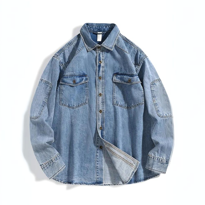 A rugged denim shirt in light blue pure cotton, featuring long sleeves, two chest pockets with flaps, and visible stitching details, laid flat on a white background.