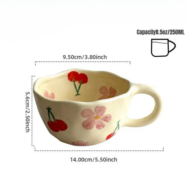 A cream-colored ceramic teacup with a large handle, decorated with pink flowers and red cherries. Reminiscent of vintage teacups, it measures 14 cm wide, 9.5 cm diameter, 5.6 cm tall, and holds 250 ml (8.5 oz).