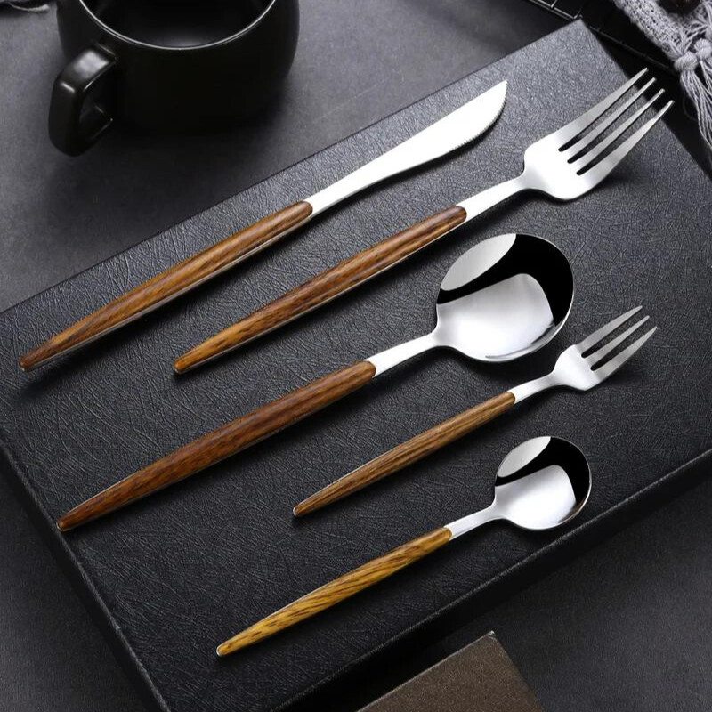 A set of five utensils—knife, two forks, and two spoons—crafted as a wooden handle silverware collection with silver tops, neatly arranged on a black textured surface. A black cup is in the background.
