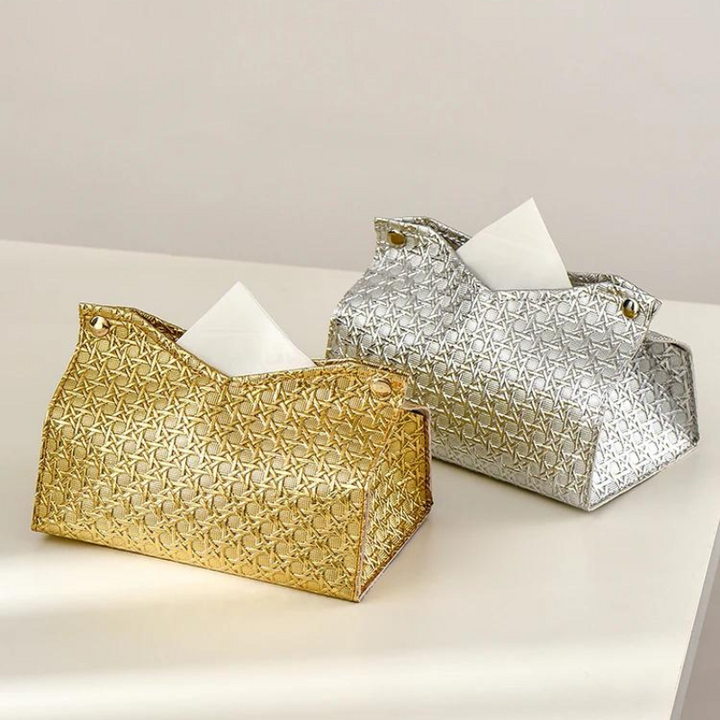 Two decorative tissue holders, the Glymmer Tissue Box in gold and silver, feature a striking geometric pattern. Side by side on a light surface, each geometric tissue box holds a white tissue partially pulled out.