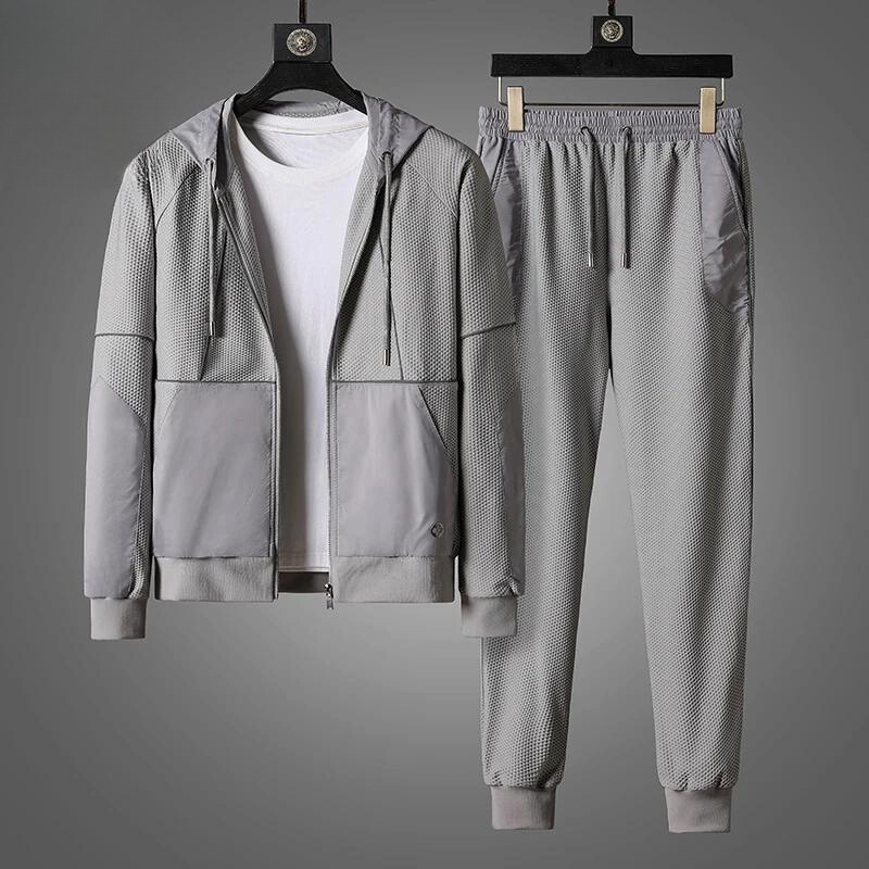 Gray activewear set featuring a zipper hoodie and matching jogger pants, displayed on hangers. Paired with a plain white T-shirt under the jacket, the moisture wicking outfit is set against a gray background.
