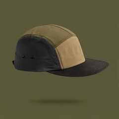 A patchwork cap with an earthtone aesthetic—olive, beige, and black panels—hovers against an olive green background, casting a faint shadow beneath it.