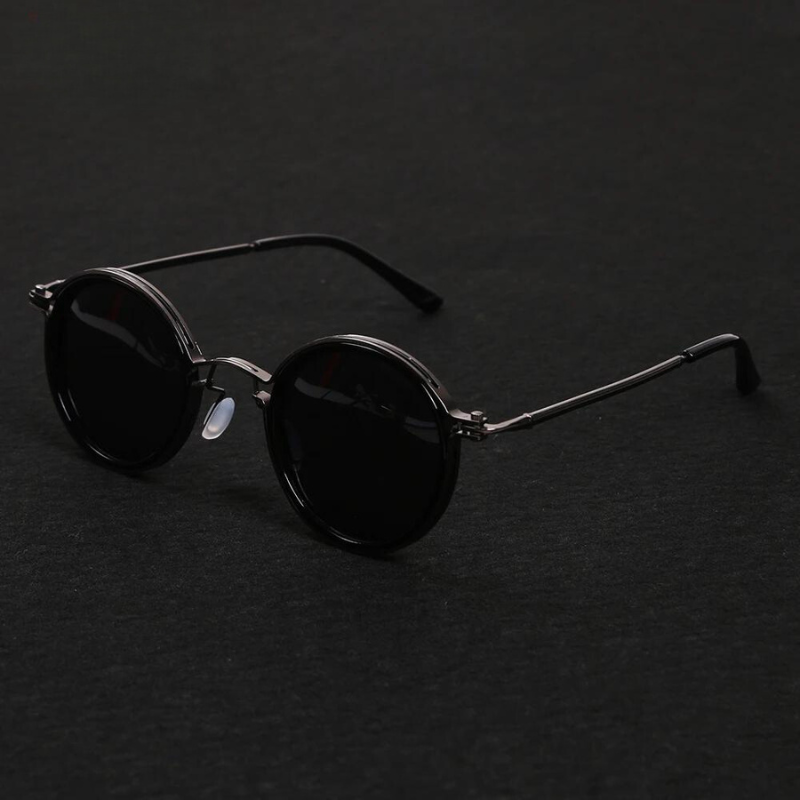 Round black Ruby Ray Sunglasses with dark lenses and thin metal frames are placed on a dark surface, their arms extended. These polarized sunglasses offer both style and enhanced UV400 protection for your eyes.