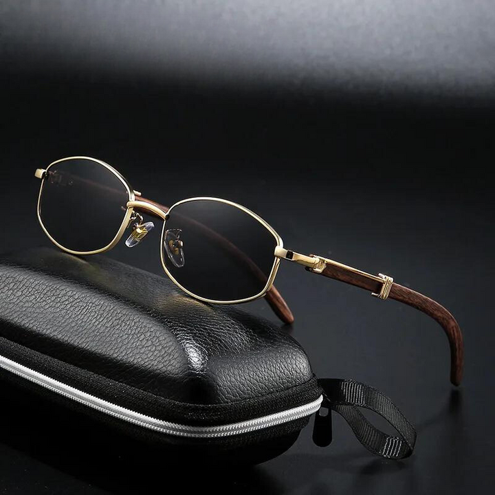 A pair of oval, gold-tone frames with brown arms rests on a closed black zippered glasses case against a dark background.