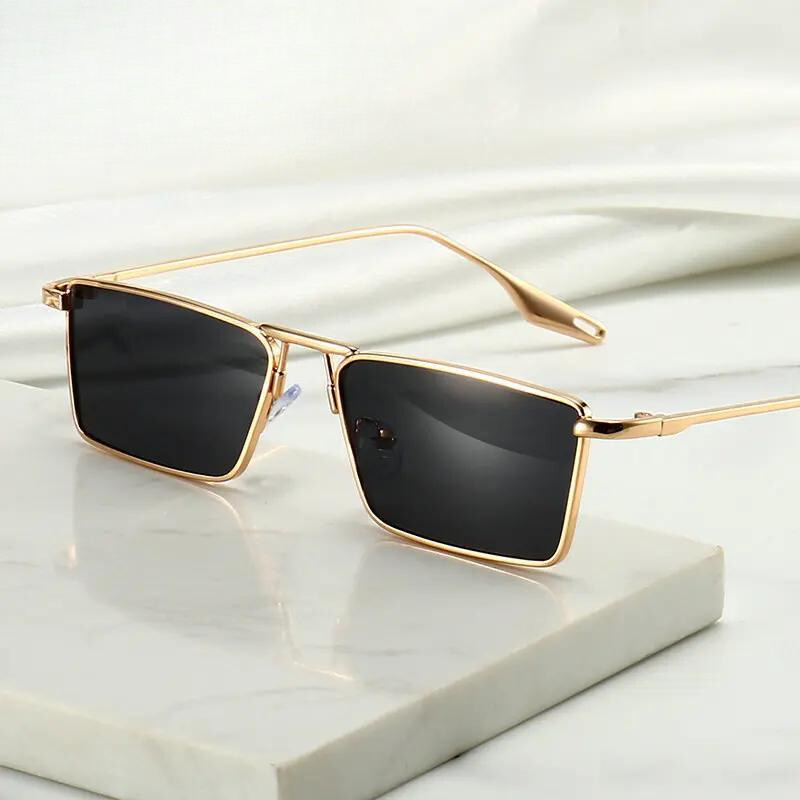 A pair of stylish Avalon Sunglasses featuring gold frames and rectangular lenses rests on a white marble surface against a soft, light-colored background.
