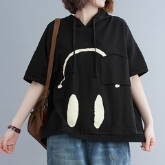 A person wearing a loose black Monday Mood hoodie with a white graphic resembling headphones on the front, paired with blue jeans and a brown shoulder bag.