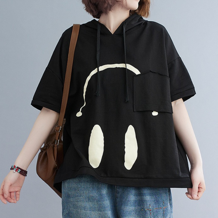 A person wearing a loose black Monday Mood hoodie with a white graphic resembling headphones on the front, paired with blue jeans and a brown shoulder bag.