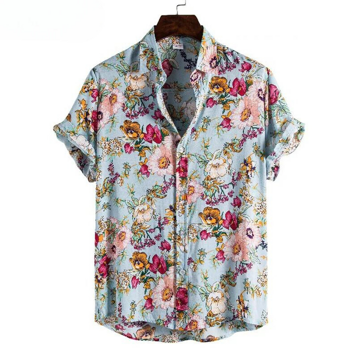 A short-sleeve, button-up, lightweight linen shirt with a light blue background features a vibrant floral pattern in pink, yellow, orange, and green. This vintage-inspired shirt is displayed on a hanger with the sleeves rolled up.