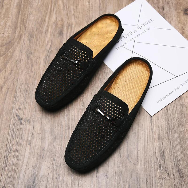 A pair of black, breathable loafers with tan insoles is placed on a wooden floor. One shoe rests partially on a white printed paper with geometric lines—ideal summer shoes for both comfort and style.