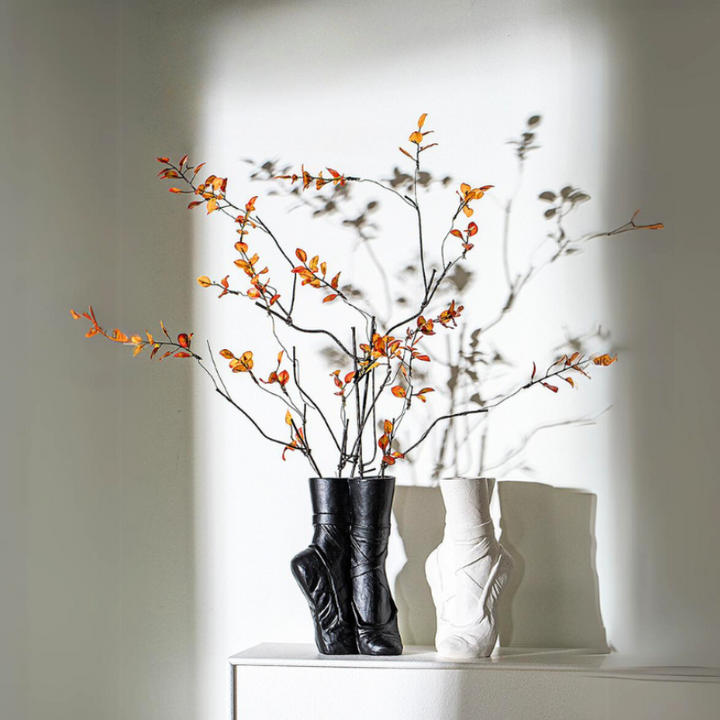 Two ballet-inspired ceramic vases, one black and one white, sit on a white surface. The black vase holds branches with small orange berries, casting dramatic shadows—perfect for contemporary chic décor.