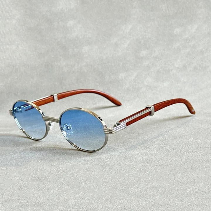 Vintage round sunglasses with silver frames, blue lenses, and brown wooden temples are displayed on a light gray textured surface. Featuring UV400 protection for stylish sun safety.