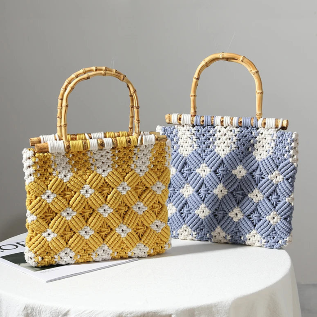 Two woven macramé handbags with bamboo handles sit on a white table. One lightweight bag is yellow and white with a diamond pattern, while the other is light blue and white with a similar design.