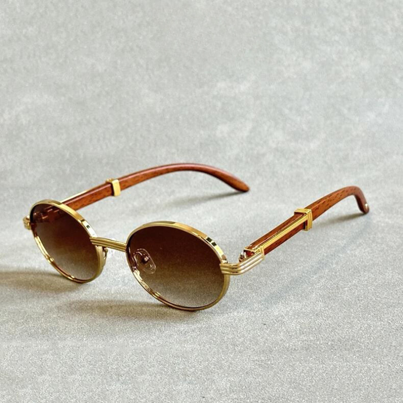 Vintage round sunglasses with gold metal frames, brown gradient lenses, and wooden temple arms are displayed on a light gray textured surface.