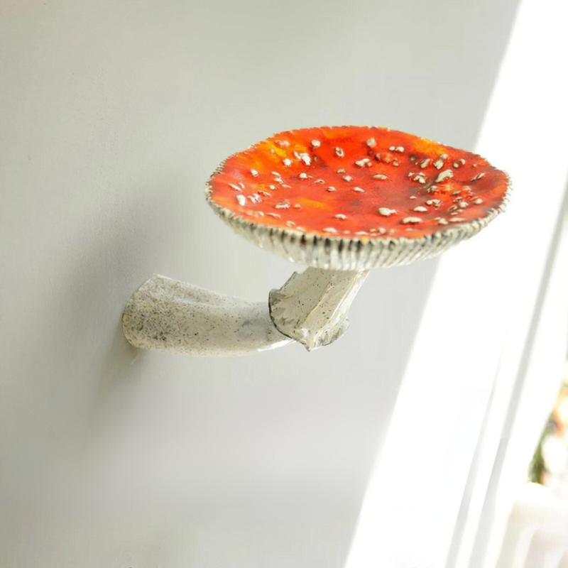 A realistic ceramic mushroom floating shelf with red and white spots is attached to a white wall, sunlight softly illuminating the scene—perfect as unique home decor with a naturalistic design touch.