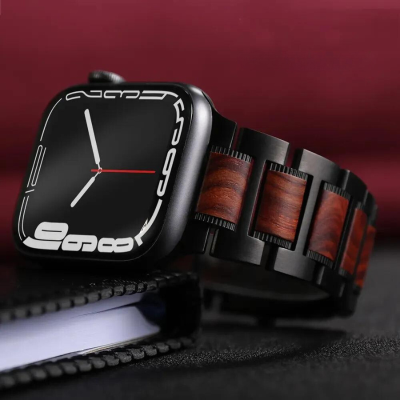 A modern smartwatch with a black case, minimalistic digital display, and an adjustable Sandalwood watch band, resting on a closed notebook against a dark red background.