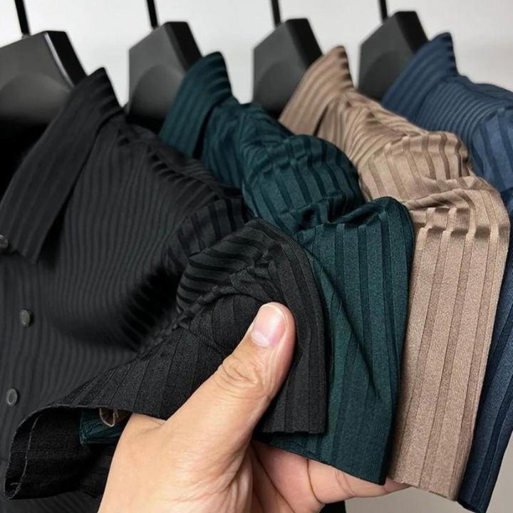 A hand holds the sleeves of four vertically striped collared shirts in black, green, brown, and blue, all hanging on black hangers—crafted from luxurious silk fabric for a premium feel and natural temperature regulation.